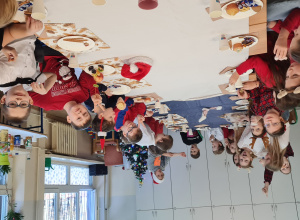 Dzieci siedzą przy stole z białym obrusem i jedzą słodkości oraz owoce.