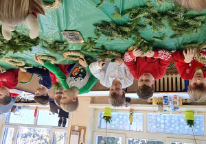 Dzieci siedzą przy stole i wbijają gałązki w wianki.