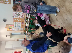 Dzieci wraz z nauczycielem i terapeutą oraz psami siedzą w kole na podłodze.