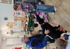 Dzieci wraz z nauczycielem i terapeutą oraz psami siedzą w kole na podłodze.