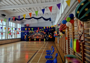Cała sala gimnastyczna wypełniona kolorowymi dekoracjami: chorągiewkami, balonami oraz stoiskami z atrakcjami.