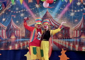 Pani Aldona Kurek oraz pani Kinga Blachowska w strojach klauna pozują do zdjęcia przy kotarze.