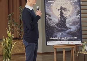 Julian recytuje wiersz na tle plakatu reklamującego konkurs.
