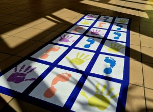 Kolorowe stopy i dłonie przyklejone do podłogi w formie maty animacyjnej.