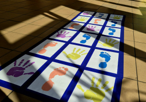 Kolorowe stopy i dłonie przyklejone do podłogi w formie maty animacyjnej.