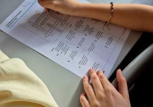 Dzieci rozwiązujące krzyżówkę na szarej ławce.