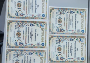 Dyplomy dla laureatów konkursu leżące na jasnym blacie ławki.
