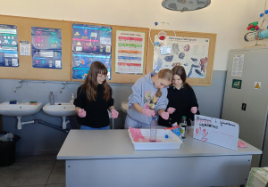 Trzy uczennice klasy 7C prezentują doświadczenie chemiczne krwawa rękawiczka.