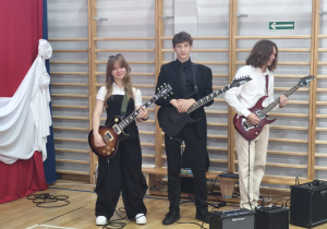 Uczniowie grają na gitarach elektrycznych podczas zakończenia roku szkolnego.
