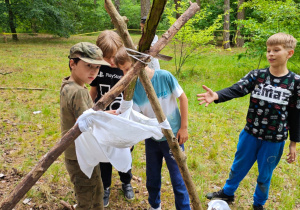 Grupa uczniów buduje filtr do wody z konarów, pieluch, trawy i piachu