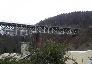 Pejzaż przedstawia most kolejowy na tle wzgórza i lasu