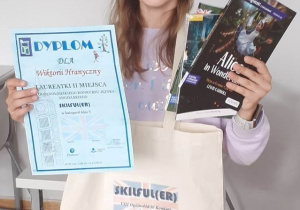 Uczennica klasy 5 a prezentuje zdobyty w konkursie dyplom i nagrody książkowe