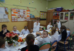 Uczniowie w strojach galowych siedzą przy świątecznie nakrytym stole.