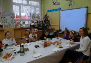 Uczniowie w strojach galowych siedzą przy świątecznie nakrytym stole.