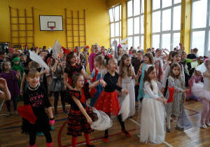 Uczniowie przebrani w stroje karnawałowe tańczą podczas balu karnawałowego.