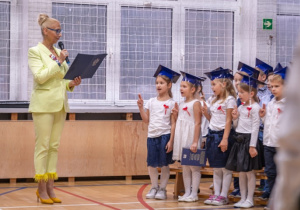 Uczniowie stoją z podniesioną prawą ręką do góry i powtarzają przysięgę odczytywaną przez panią dyrektor Beatę Pietrzak