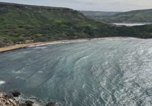 Krajobraz Malty: zatoka morska, kamienista plaża i zielone wzgórze