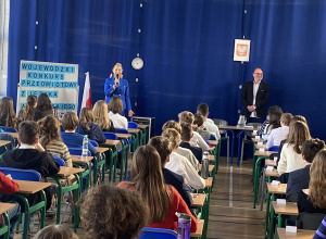 Pani dyrektor Beata Pietrzak wita uczestników konkursu siedzących w ławkach na sali gimnastycznej