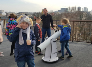 Uczniowie stoją na dachu Planetarium obok teleskopu i słuchają opowieści pracownika o działaniu urządzenia