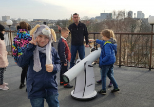 Uczniowie stoją na dachu Planetarium obok teleskopu i słuchają opowieści pracownika o działaniu urządzenia