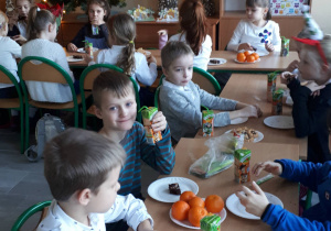 Uczniowie siedzą przy uroczyście nakrytym stole i jedzą słodki poczęstunek.