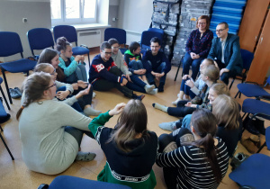 Uczniowie siedzą w kole na podłodze i rozmawiają z parą psychologów.