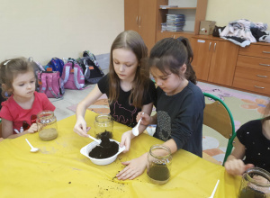 Uczennica napełnia słoik ziemią wsypując ją plastikowa łyżką