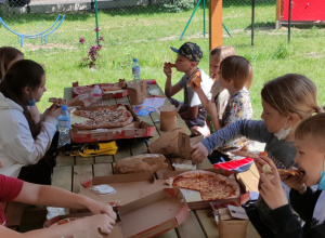 Uczniowie siedzą w drewnianej altanie ogrodowej i jedzą pizzę