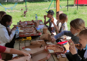 Uczniowie siedzą w drewnianej altanie ogrodowej i jedzą pizzę