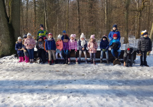 Uczniowie klasy 1. a pozują do zdjęcia siedząc na balu drewna