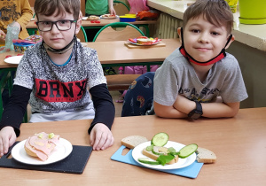 Dwaj uczniowie prezentują kanapki wykonane z wędliny i warzyw.