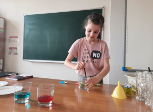 Uczennica miesza pipetą kolorową ciecz w szklanym pojemniku.