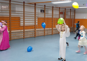 Uczennice w strojach karnawałowych tańczą z balonami podczas balu karnawałowego.