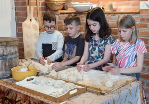 Czworo uczniów wyrabia chleb na wielkich stolnicach.