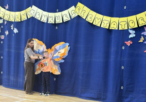 Uczeń podczas recytacji wiersza stoi na tle dekoracji z motylami.