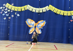 Uczennica podczas recytacji wiersza stoi na tle dekoracji z motylami.