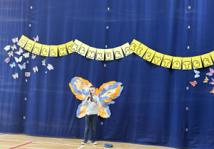 Uczeń podczas recytacji wiersza stoi na tle dekoracji z motylami.