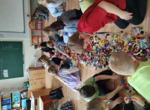 Uczniowie klasy IIB wspólnie budują modele ryb, wykorzystując rozłożone na podłodze klocki Lego.