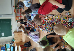Uczniowie klasy IIB wspólnie budują modele ryb, wykorzystując rozłożone na podłodze klocki Lego.