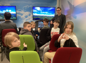 Uczniowie siedzą przed symulatorem lotu.