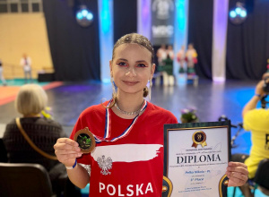 Nikola ubrana w czerwona koszulkę z napisem Polska prezentuje zdobyty medal i dyplom.