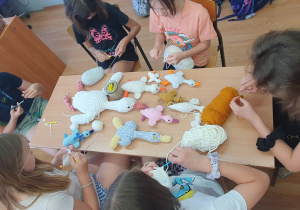 Uczniowie siedzą wokół ławki i szydełkują maskotki.