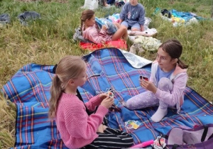 Sześć uczennic siedzi na kocach i gra w przyniesione gry.