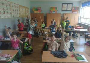 Uczniowie siedzą w ławkach i jedzą lody.