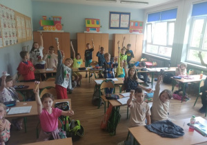 Uczniowie siedzą w ławkach i jedzą lody.