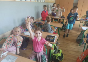 Uczniowie siedzą w ławkach i jedzą lody.