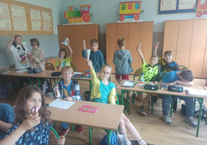 Uczniowie siedzą w ławkach i jedzą lody.