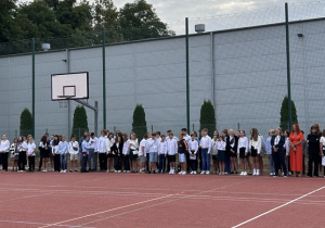 Uczniowie klas 4-8 wraz z wychowawcami na boisku szkolnym podczas uroczystości rozpoczęcia roku szkolnego.