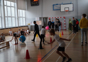 Uczniowie klasy 2.A na sali gimnastycznej biorą udział w zabawach sportowych przygotowanych przez uczniów klasy 6. A.