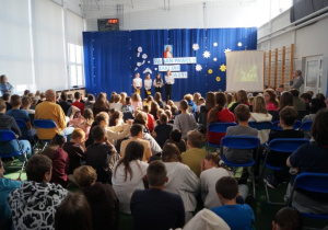 Uczennice z klasy 7 a recytują wiersz stojąc na tle granatowej dekoracji.